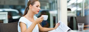 UKSBA__young-woman-reading-a-newspaper-and-drinking-coffee